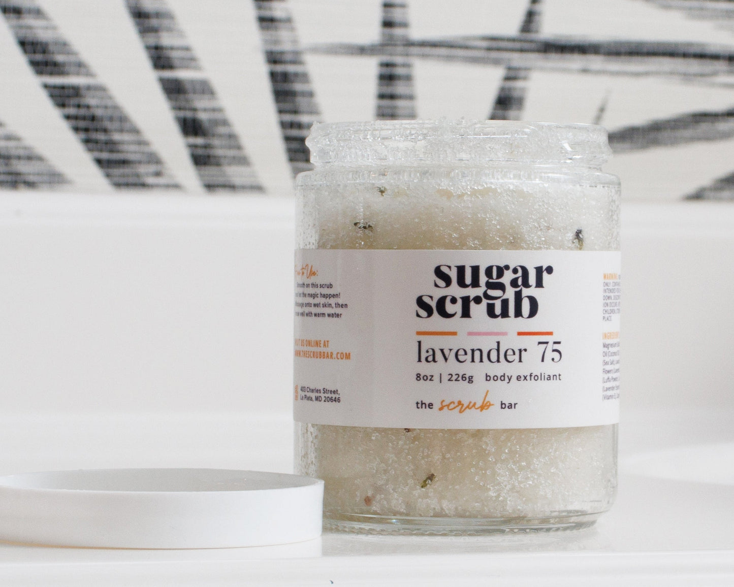 Jar of sugar scrub labeled lavender 75' on a white background with black abstract patterns.