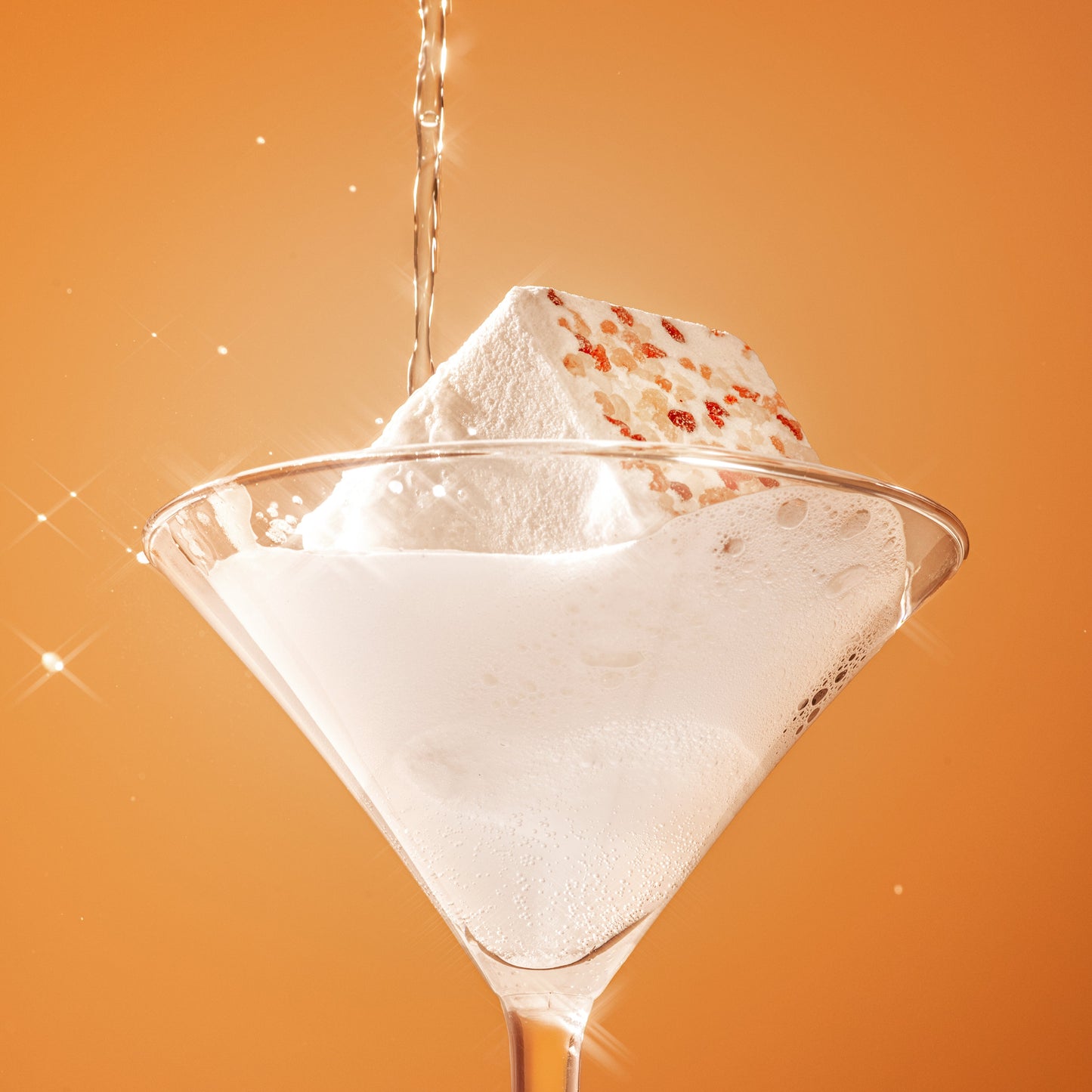 The Scrub Bar’s eucalyptus bath bomb fizzes in a martini glass with foamy bubbles and visible Himalayan salt rocks.