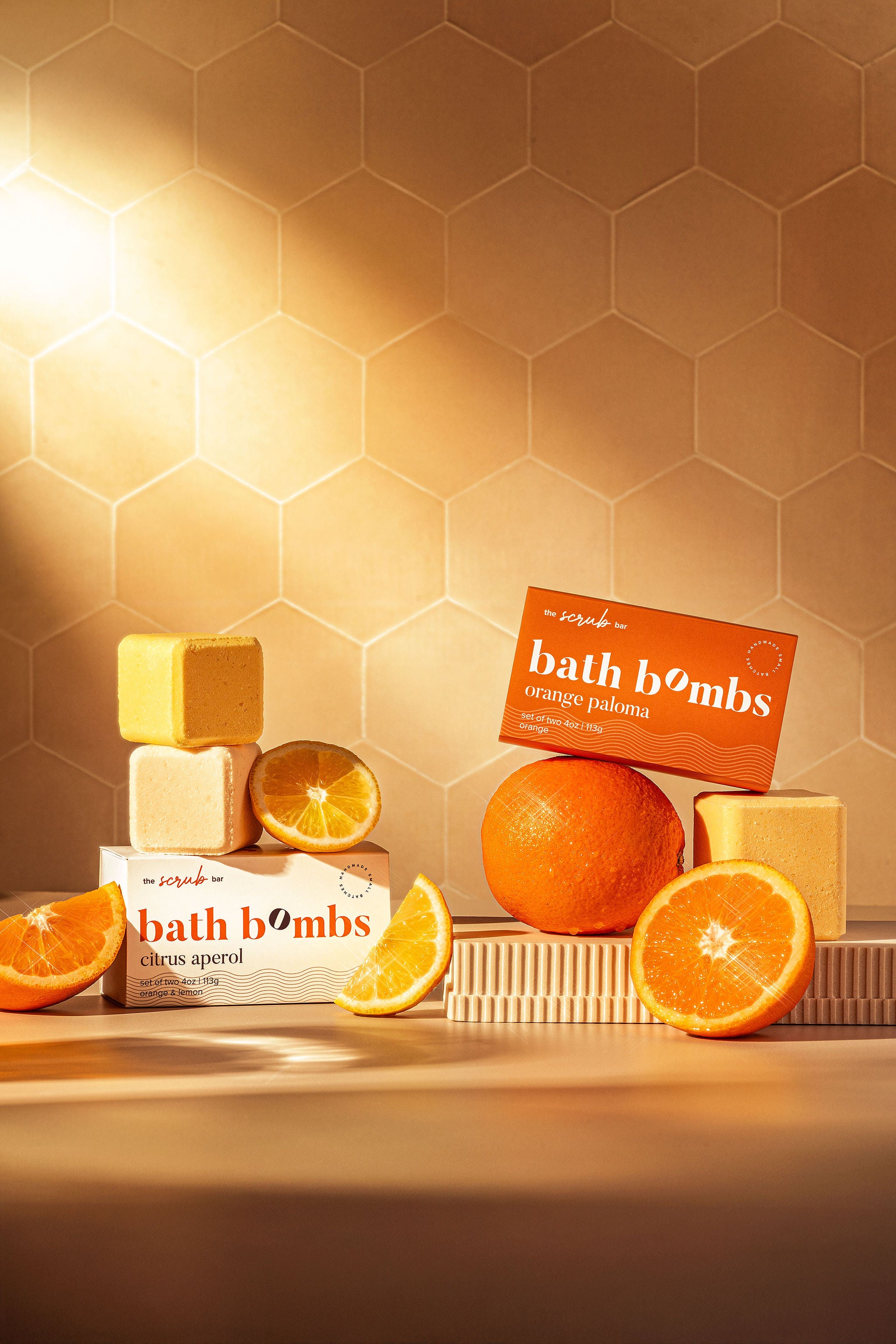 Colorful bath bomb gift boxes by The Scrub Bar, in citrus scents, styled with yellow lemon and orange slices in a fresh, sunlit setting.